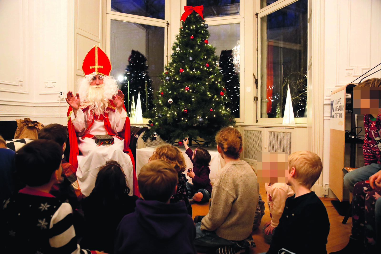 Der Nikolaus erzählt am Weihnachtsbaum, rund zwanzig Kinder hören zu