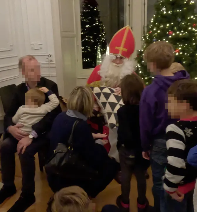 Nikolaus sitzt vor dem Weihnachtsbaum. Vor ihm stehen Kinder in der Schlange und eine Dame kniet vor ihm. Die Dame signalisiert "Stopp" mit ihren Händen. Neben Nikolaus sitzt ein Vater mit Kind auf dem Schoß und guckt kritisch. Gesichter verpixelt.