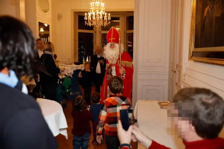 Nikolaus steh im Festsaal. Vor ihm einige Kinder zu ihm aufschauen. Hinder den Kindern beglückte und fotografierende Eltern.