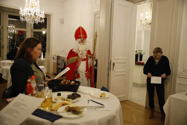 Nikolaus steht inmitten des Saales und schaut kritisch. Zwei Frauen singen.
