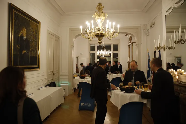 Festsaal der Kondrad-Adenauer-Stiftung vom Standort des Nikolaus' fotografiert. Etwa 20 Erwachsene stehen an Stehtischen, essen und trinken Bier oder unterhalten sich.